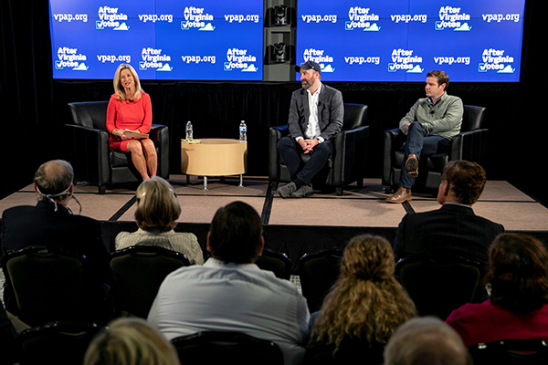 Three people on a stage in front of a blue sign.