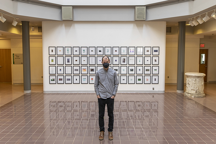 Michael McDermott is wearing a mask and standing in front of part of his exhibit of found images and text