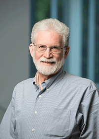 This headshot of Jonathan Goldman in a light-blue, button-down shirt and glasses, for his faculty profile at George Mason University. 