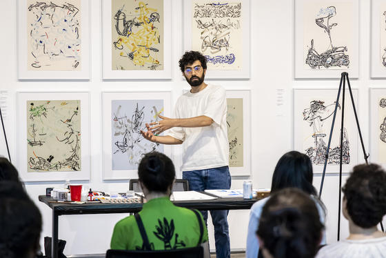 bearded man standing before artwork talking to audience